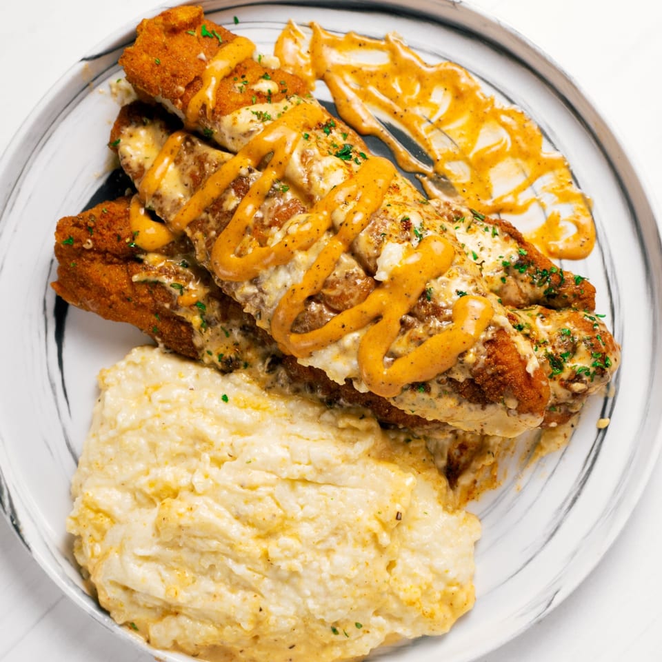 Fried fish fillets drizzled with creamy sauces and fresh herbs, served with a side of grits.